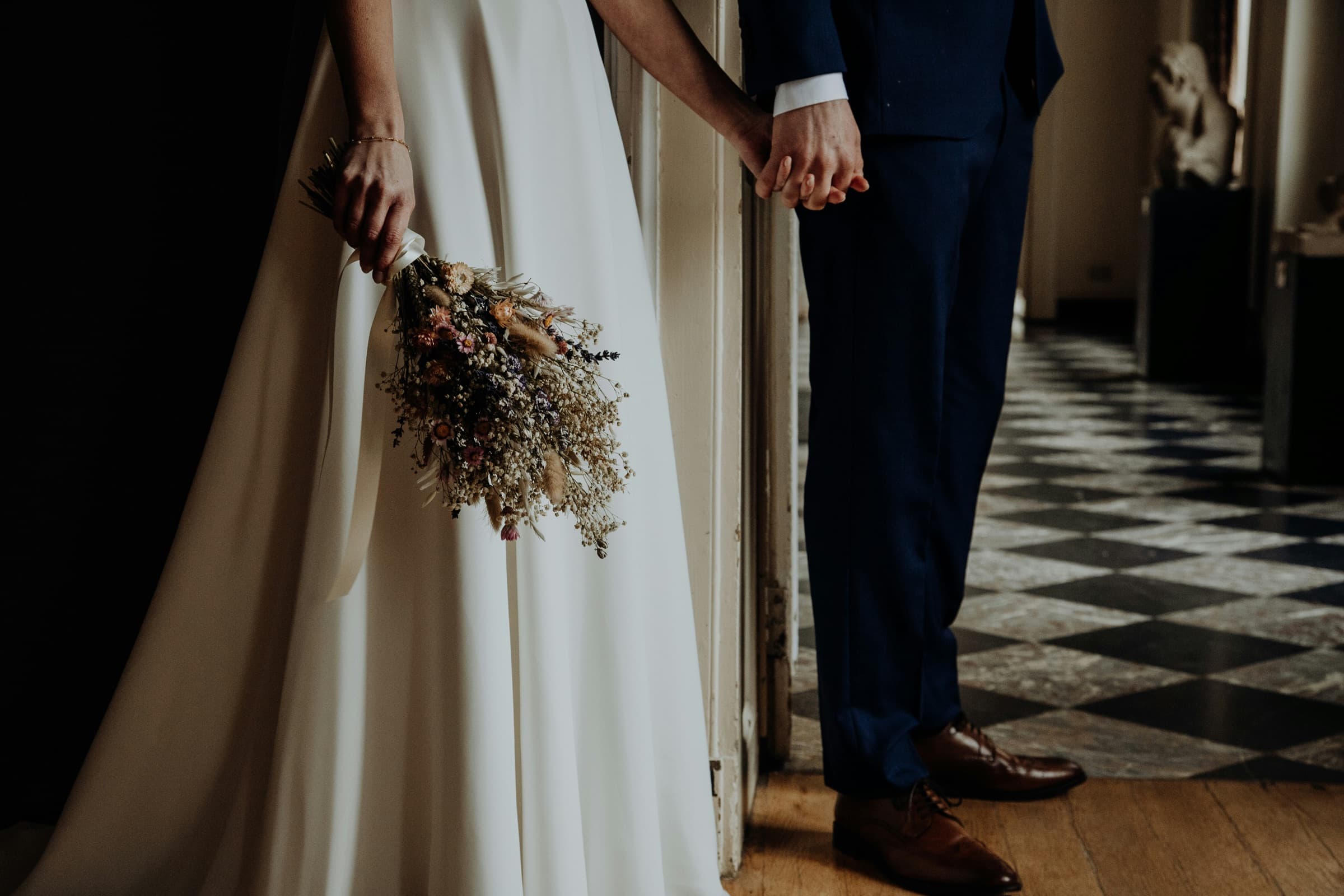 Couple le jour de leur mariage, mains jointes avec un bouquet de fleurs séchées